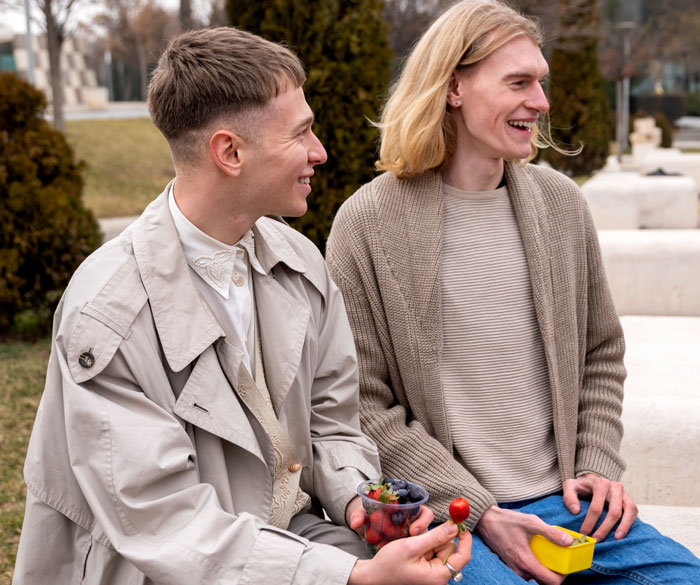 Two young men sitting outside smiling, one holding a container of berries, illustrating a dorm inspector visit.