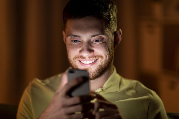 Young man looking at phone with a smirk, embodying arrogance while comparing his devoted girlfriend to another man's wife.