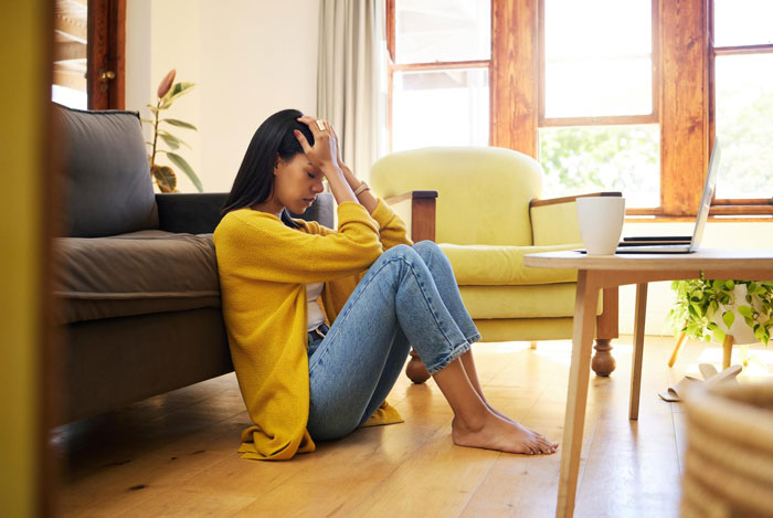 Young woman sitting on the floor looking stressed after arrogant guy ruthlessly compares his devoted girlfriend to another woman