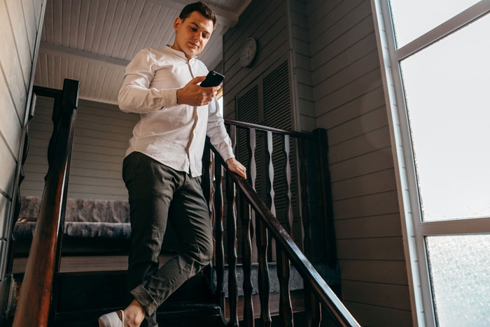 Young man in white shirt on stairs looking at phone, illustrating a cunning guy orchestrating a loyalty test scenario.