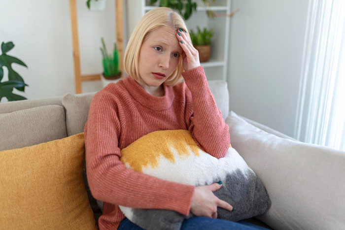 Young woman looking distressed on a couch, holding a pillow, reflecting symptoms of imagining things and hearing voices.