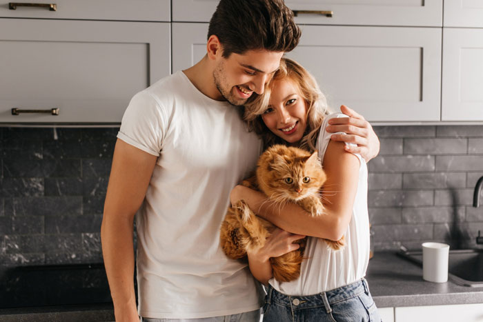 Couple embracing in kitchen holding a fluffy orange cat, sharing a moment of breaking family tradition getting dog.