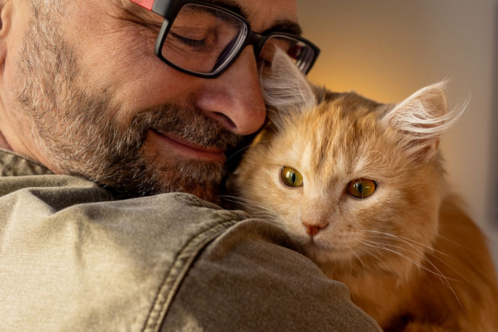 Man with glasses hugging an orange cat indoors, illustrating breaking family tradition of getting dog.