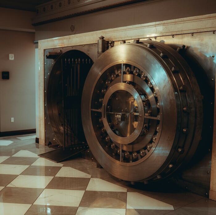 Large open bank vault door with intricate locking mechanism in a dimly lit room, evoking haunted place atmosphere.