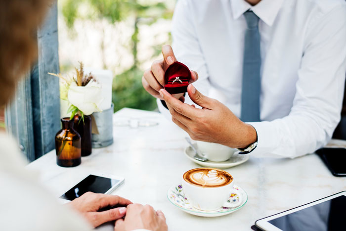 Man in a white shirt and tie proposes with a diamond ring, highlighting a relationship red flag and ring complaint.