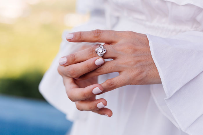 A person's hands, with manicured nails and an engagement ring on the left ring finger, illustrating a proposal.
