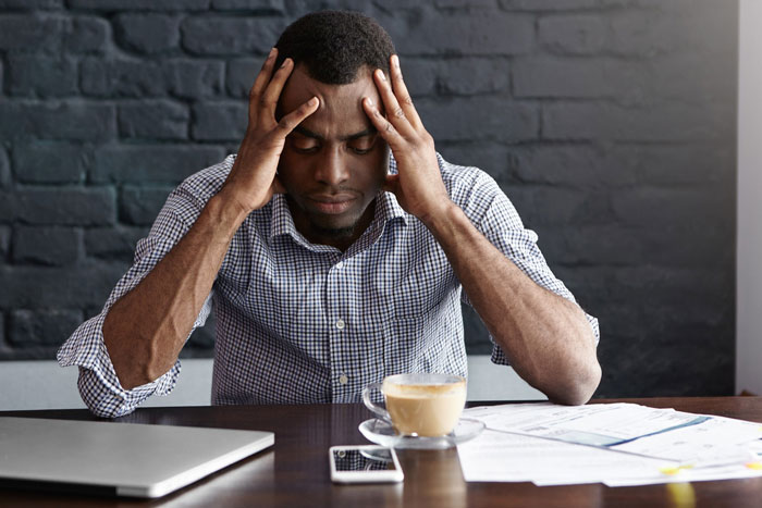 Man holding his head in frustration while sitting at a table with documents and laptop, reflecting brother inherited land money issues