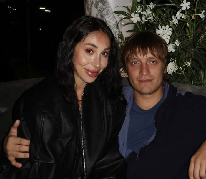 Young man and woman sitting closely together outdoors with plants in background, police release disturbing update in Bali case.