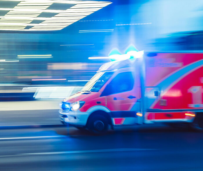 Ambulance with flashing lights speeding on urban street at night, related to horrifying video fatal push incident.