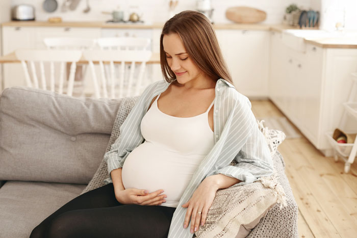 Pregnant woman sitting on a couch, gently holding her belly, symbolizing changing baby name during pregnancy.