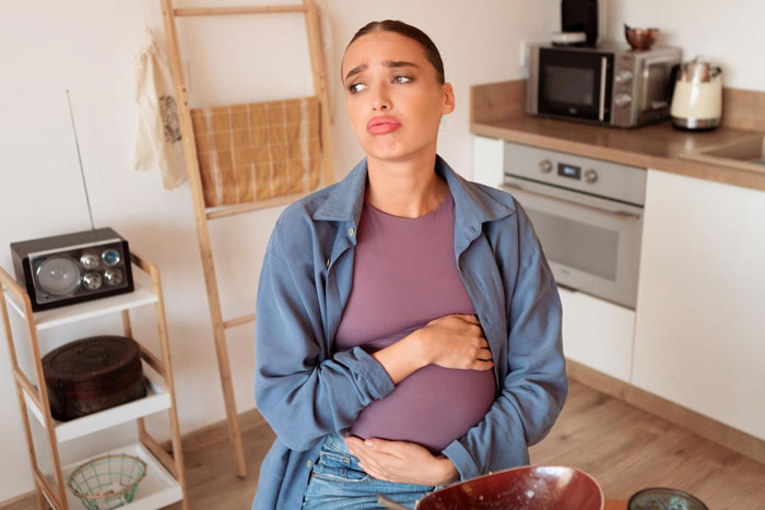 Pregnant woman in kitchen looking concerned while holding belly, reflecting on changing baby name secretly pregnant decisions.