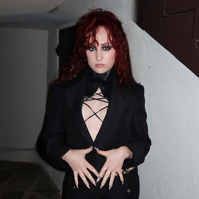 Chappell Roan posing in black attire with red hair, linked to the security guard and Jude Law's daughter debacle.