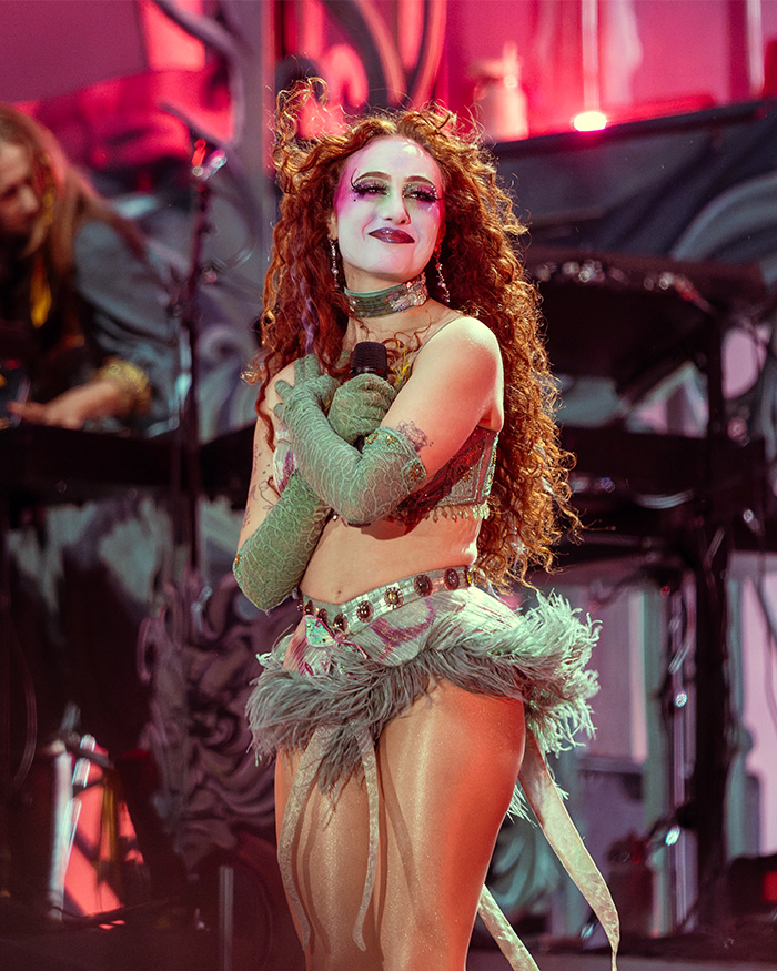 Chappell Roan performing on stage in an elaborate costume amid dramatic lighting and musical instruments. Chappell Roan performing on stage in an elaborate costume amid dramatic lighting and musical instruments.