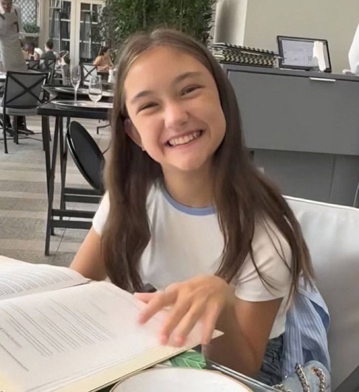 Smiling young girl sitting at a table reading a book, related to Jude Law's ex calling out Chappell Roan.