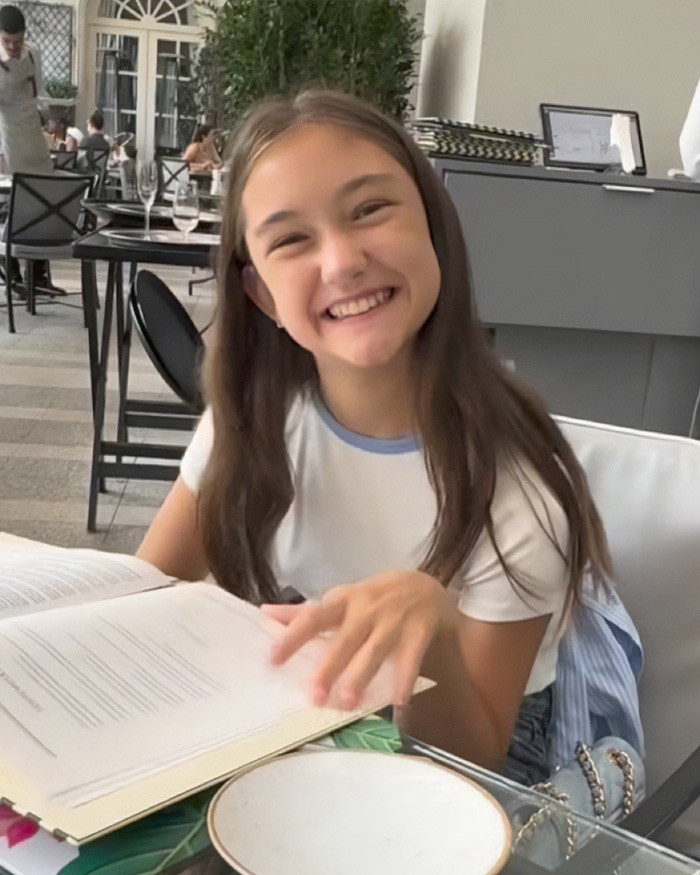 Smiling young girl sitting at a table with an open book, unrelated to Chappell Roan backlash or Jude Law's daughter. Smiling young girl sitting at a table with an open book, unrelated to Chappell Roan backlash or Jude Law's daughter.