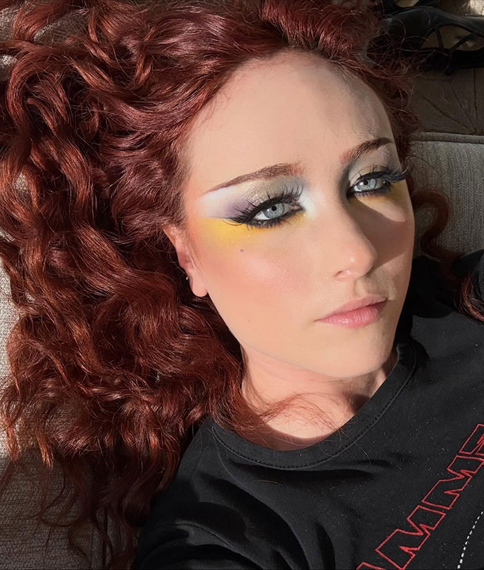 Chappell Roan with curly red hair and vibrant eye makeup lying down, highlighting her background and fan attention.