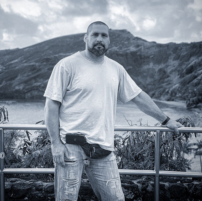 Security guard involved in Jude Law’s daughter incident posing outdoors near a railing with mountainous landscape behind. Security guard involved in Jude Law’s daughter incident posing outdoors near a railing with mountainous landscape behind.