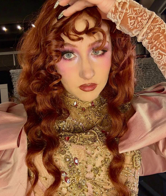 Chappell Roan with intricate makeup and curly red hair, wearing a detailed gold and pink embellished outfit.