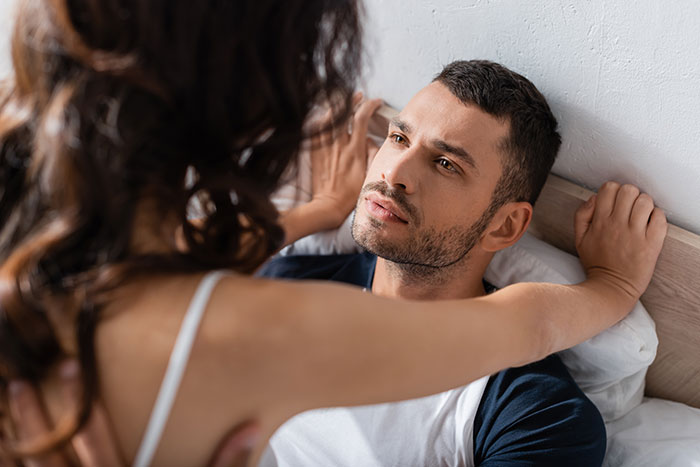 Woman confronts married man in bed, showing tension and conflict in an intimate setting.