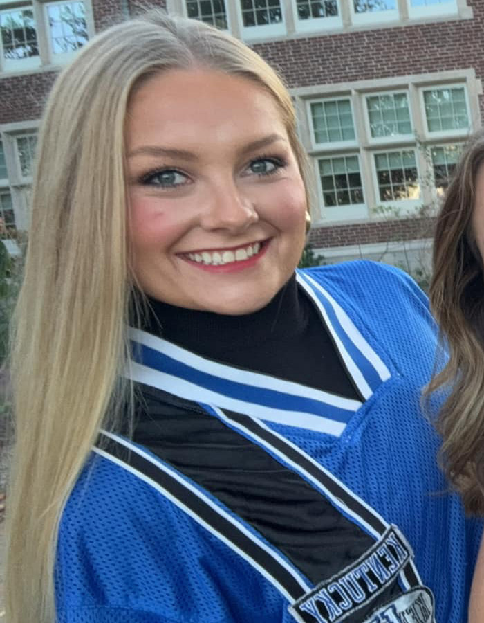 Cheerleader Laken Snelling wearing blue uniform smiling outdoors with building windows in the background.