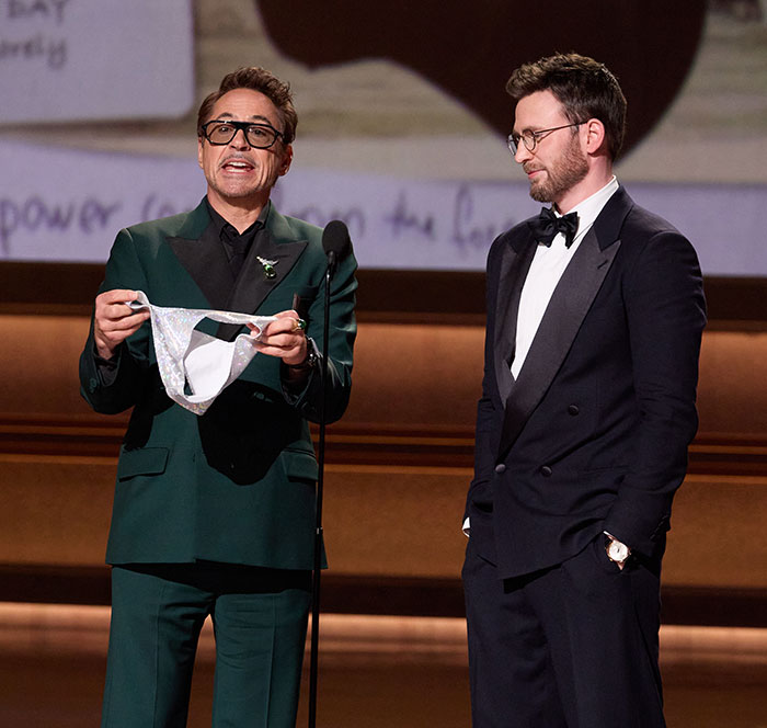 Two men in tuxedos on stage at the Oscars, one holding a sparkling silver item, capturing cringe moments at the 2026 Oscars.