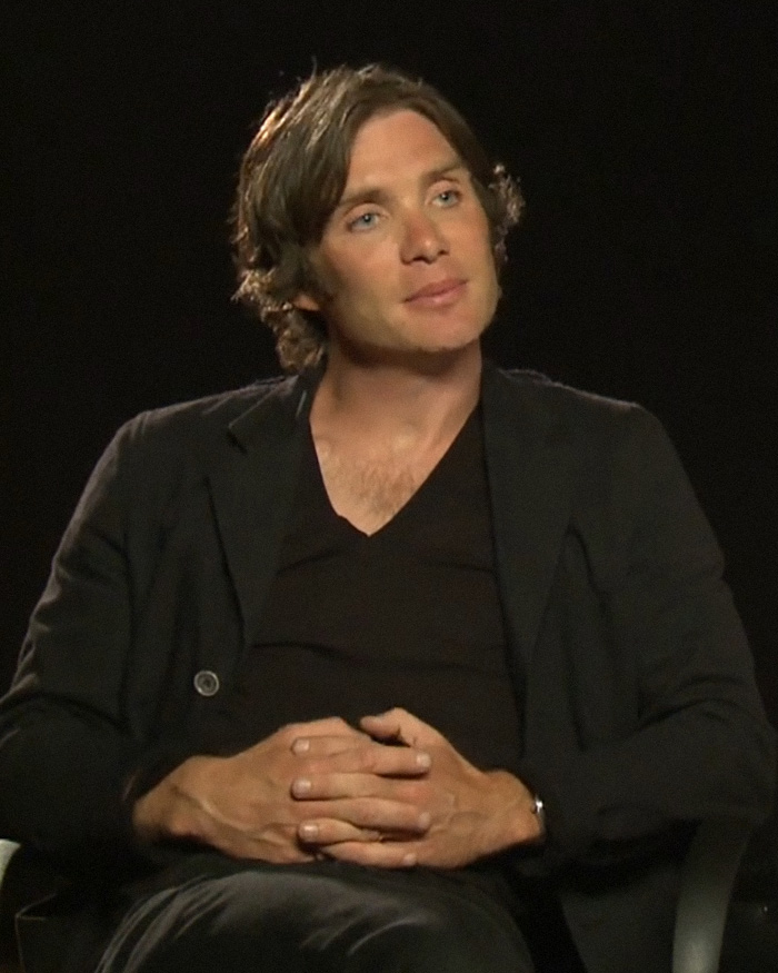 Cillian Murphy seated in a black blazer and shirt against a dark background, sparking debate over how he&rsquo;s aged.