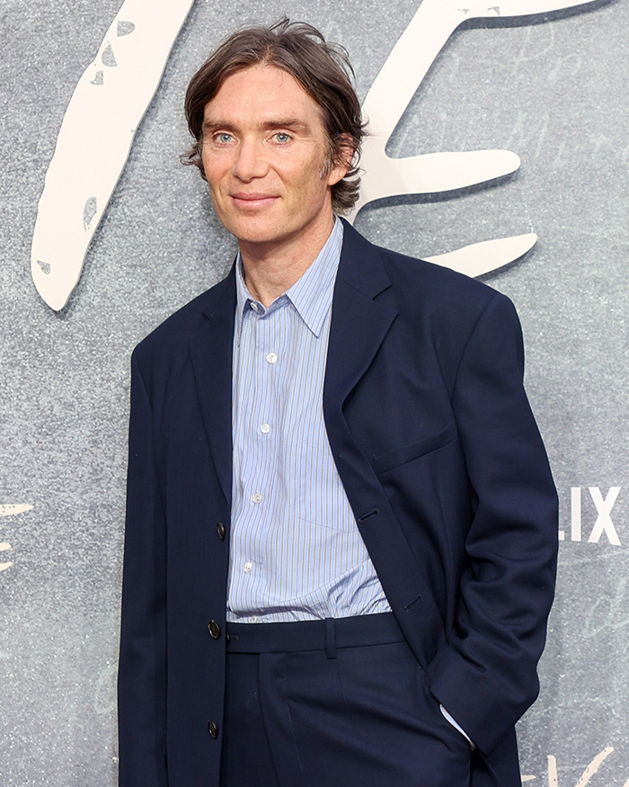 Cillian Murphy in a navy suit and striped shirt posing at an event sparking debate over how he has aged.
