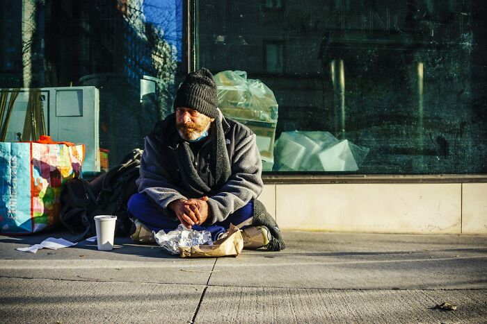 Homeless man sitting on sidewalk with food and belongings, illustrating moments people destroyed their own lives.