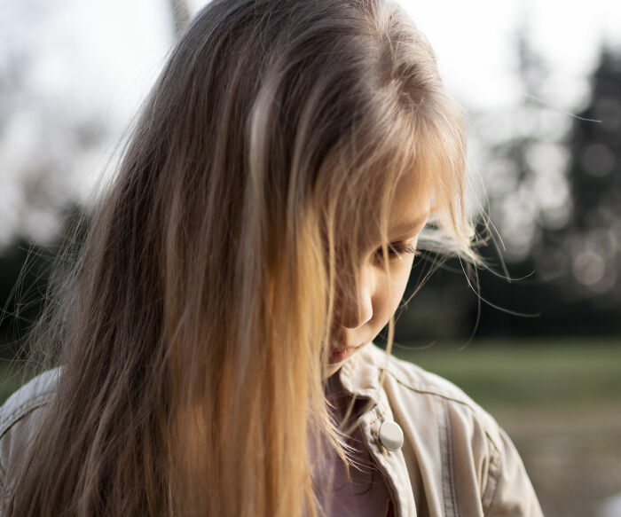 Sad young girl outdoors looking down with blurred background, related to mom arrested and obscene gesture case.