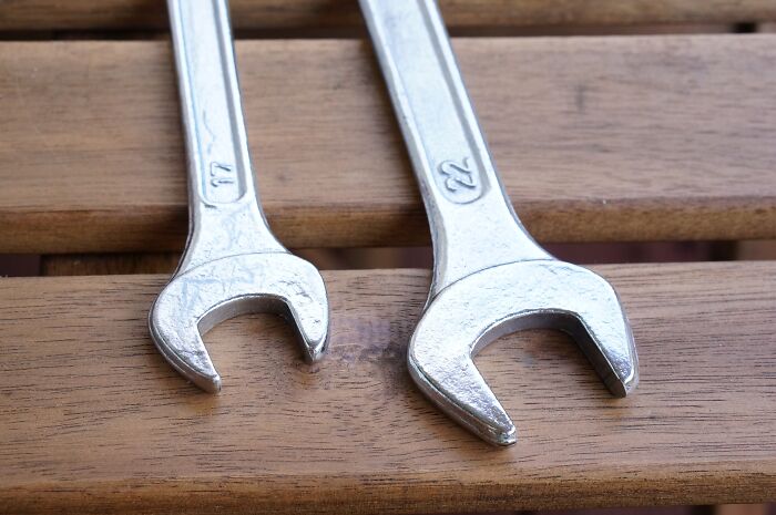 Two metal wrenches on a wooden surface symbolizing men shooting themselves in the foot with mansplaining.