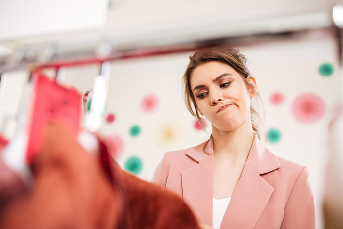 Woman in pink blazer looking displeased while examining clothes, symbolizing office bully exposed and losing jobs scenario.