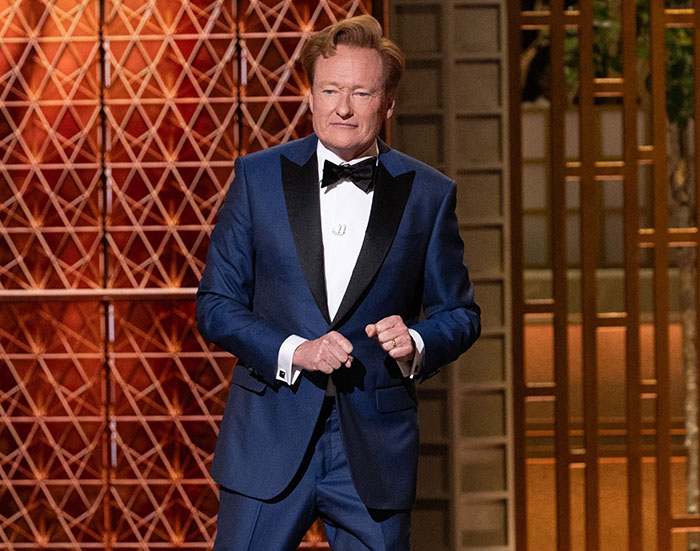 Host in a blue tuxedo on stage at the 2026 Oscars during one of the most painfully cringe moments of the event.