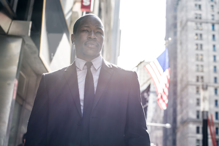 Man in a suit standing on a city street with sunlight and an American flag, representing interesting rabbit holes.
