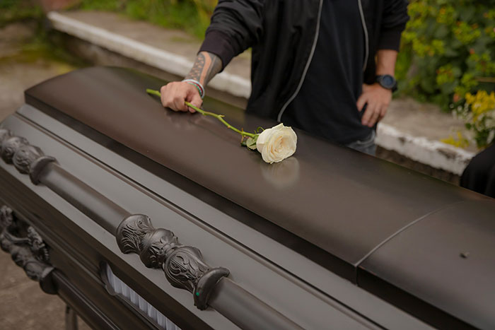 Person mourning at a funeral holding a white rose on a black casket, highlighting corrupt businesses' impact on trust.
