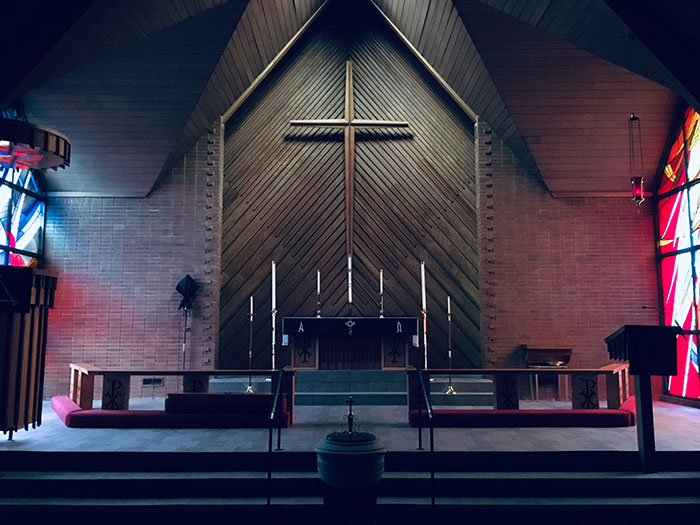 Interior of a place of worship with stained glass, candles, and a large cross, highlighting businesses usually more corrupt than known.