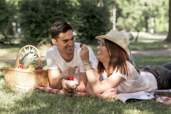 Couple enjoying a picnic outdoors, sharing fruit and smiling on a sunny day, highlighting mansplaining concept.