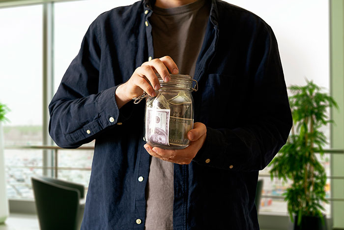Person holding a glass jar filled with cash, symbolizing revenge to coworkers who deserved it at the office.