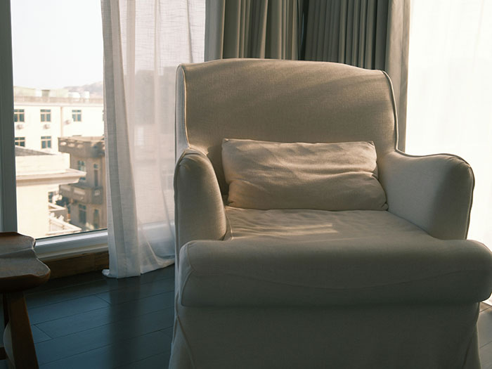 Beige armchair near window with sheer curtains in a modern room, illustrating revenge to coworkers who deserved it concept.