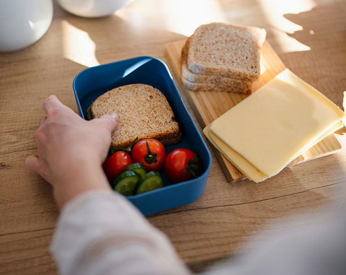 Hand placing a sandwich with tomatoes and cucumbers in a lunchbox, symbolizing revenge to coworkers who deserved it.