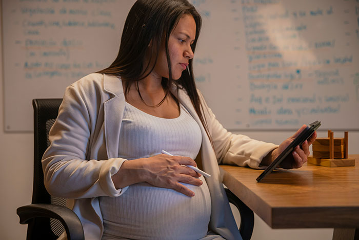 Pregnant woman working late at desk, focused on tablet, illustrating stories of revenge against coworkers who deserved it.