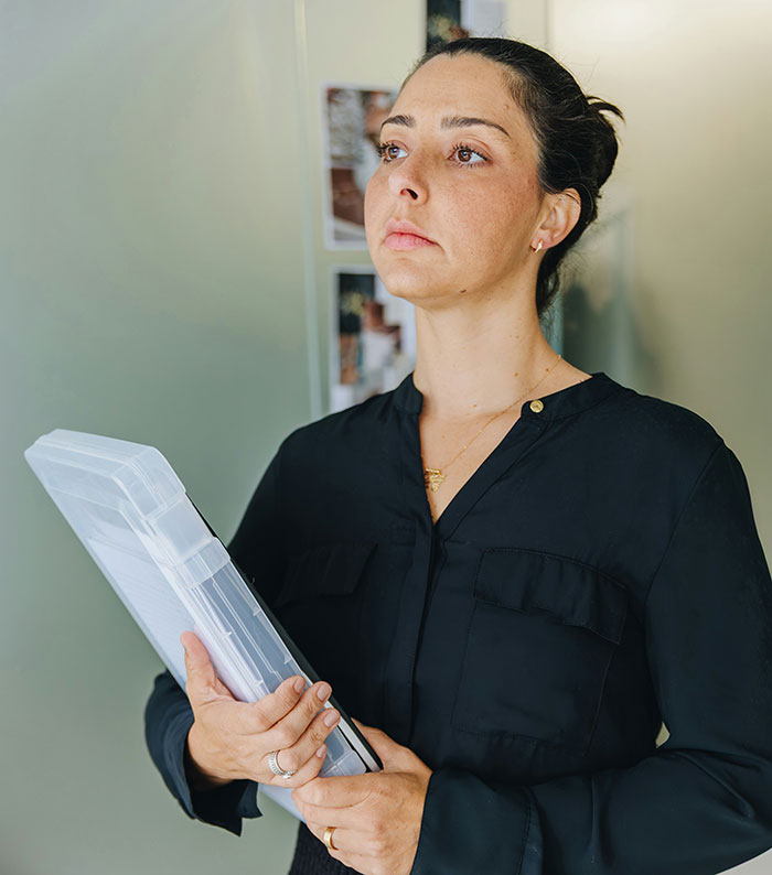 Woman in black shirt holding files, looking determined after serving revenge to coworker who deserved it.