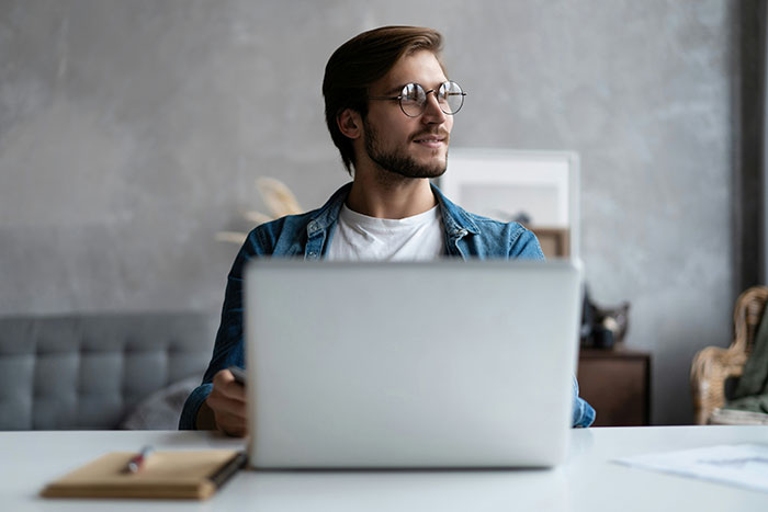 Man wearing glasses working on laptop at desk, symbolizing revenge to coworkers who deserved it in office setting.