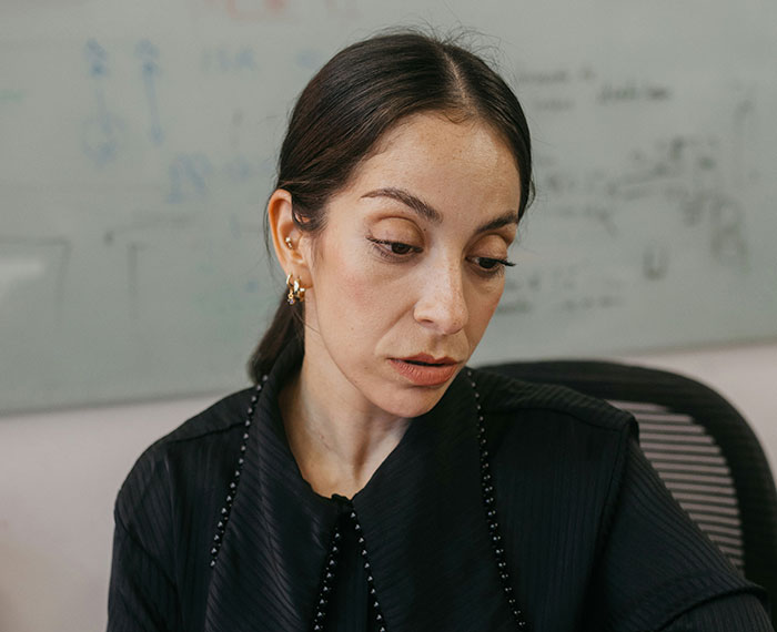 Woman in office setting looking down thoughtfully, representing revenge to coworkers who deserved it concept for workplace conflicts.