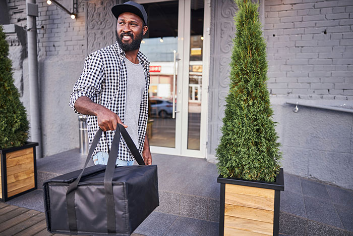 Man carrying a black delivery bag outside a building, illustrating revenge served to coworkers in a real-life scenario.