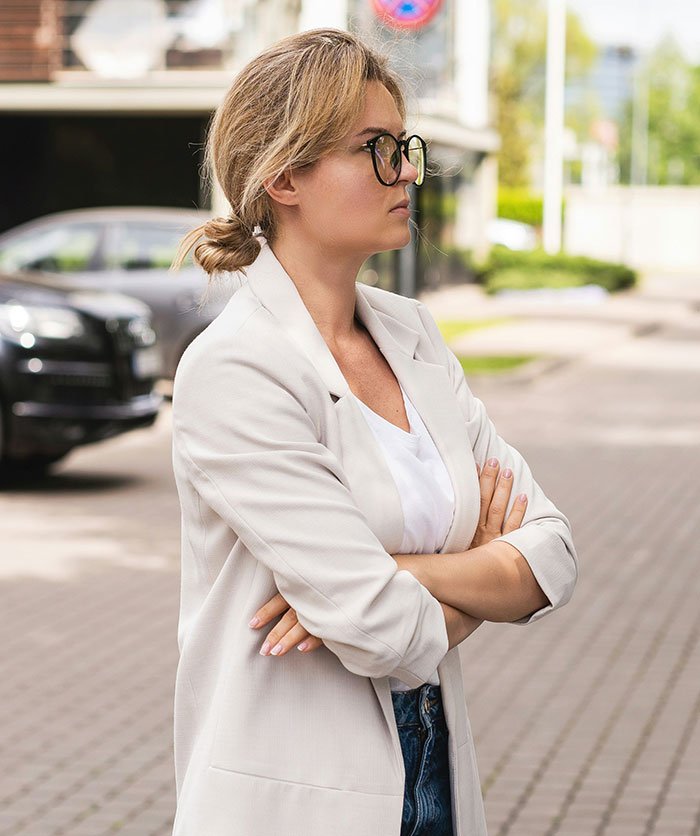 Woman in glasses and blazer with arms crossed, showing determination and confidence in a revenge to coworkers scenario.