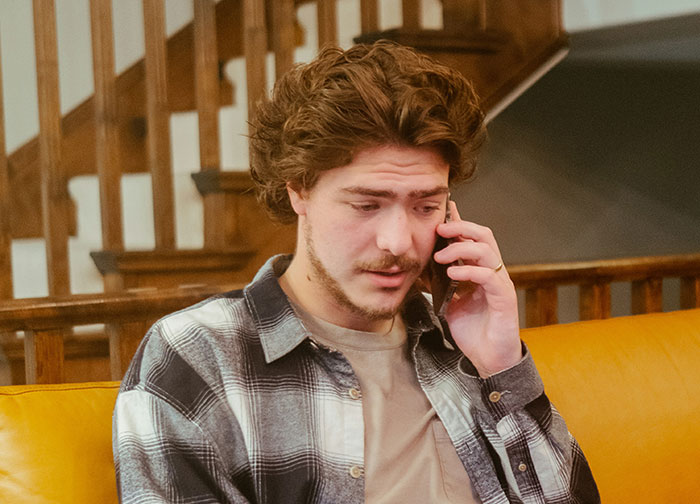 Young man on a phone call at home, showing concern in a casual setting related to catching ex cheating stories.