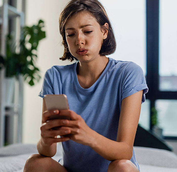 Young woman in blue shirt looking shocked while checking her phone, illustrating weird ways people caught their exes cheating.
