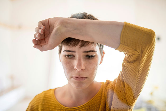Young woman in a yellow shirt looks distressed while wiping sweat from her forehead, relating to how people caught their exes cheating.