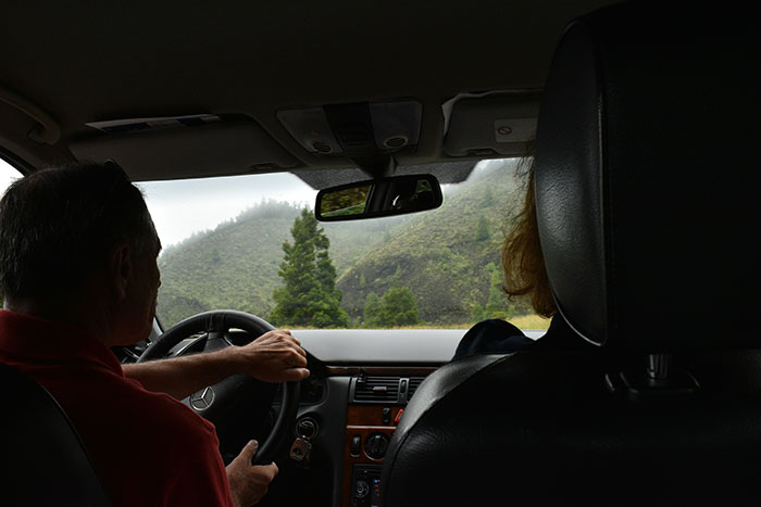 Man driving a car with a passenger, surrounded by foggy mountains, illustrating stories about catching exes cheating.