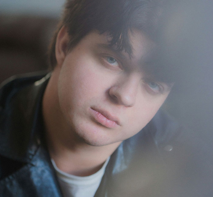 Young man with dark hair and blue eyes looking through a foggy window, representing catching exes cheating stories.